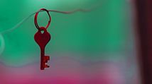Key hanging from a wire on a green and pink background