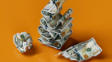 Artfully arranged $100 bills in a stack, plus one crumpled and one torn. They are presented on a bright orange background.