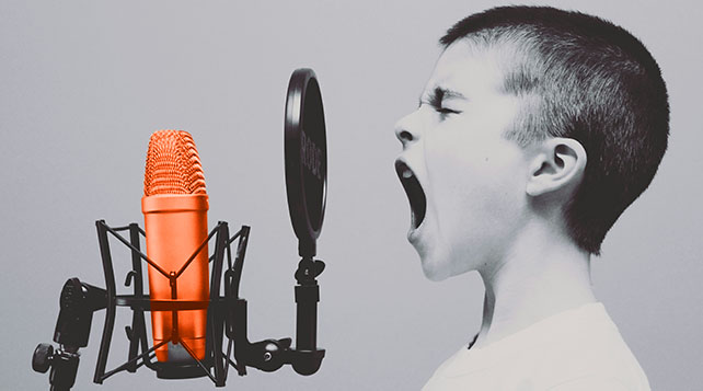 black and white photo of a young boy yelling through a screen at an orange microphone