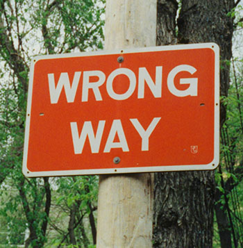 Orange sign saying WRONG WAY nailed to a grey pole