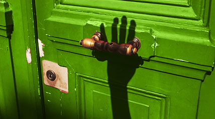 Green door with shadow of a hand reaching toward the handle to open it